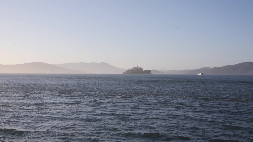 A large body of water with a rocky island straight ahead and a boat to the right