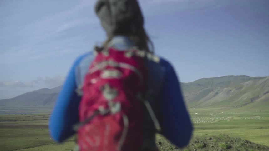 A woman with a backpack hikes through a valley