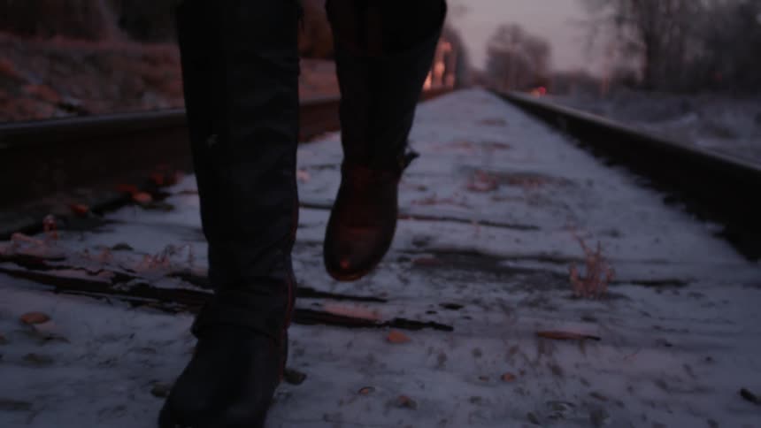 A person wearing leather boots walks down snow covered train tracks