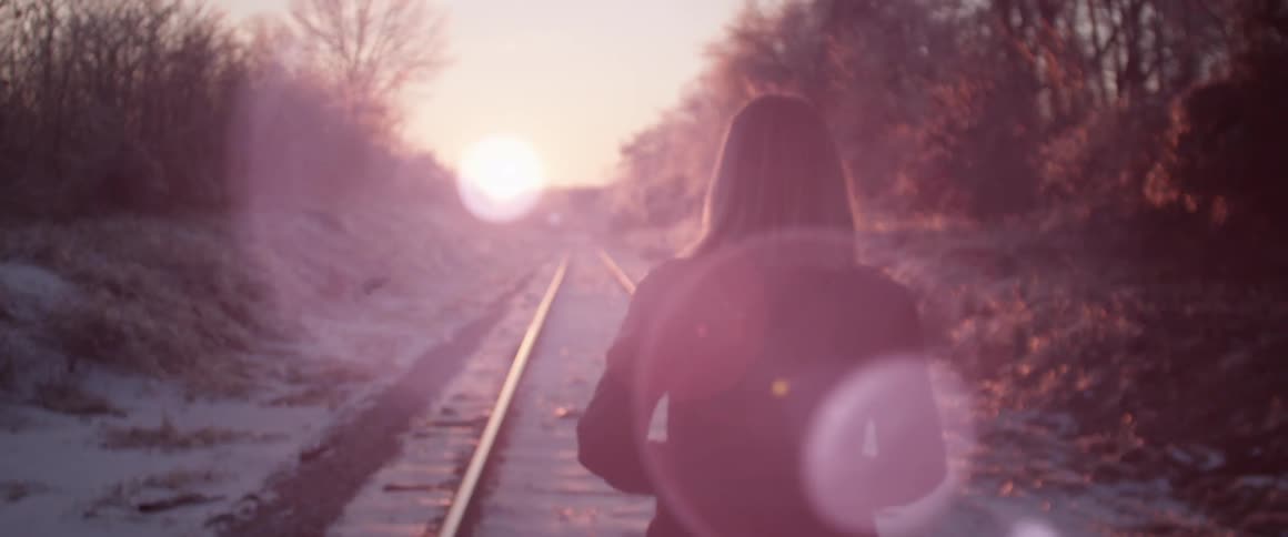 A woman walks in the train road towards the sun