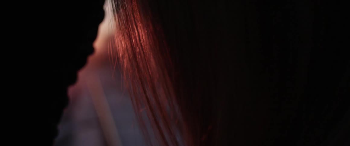 Girl runs hand through hair while standing on train tracks during sunset