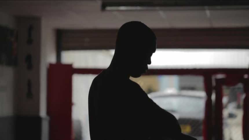 An young man shown in silhouette in a gym wrapping his hands in preparation for a workout