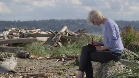 Woman sitting on a tree stump writing in a book
