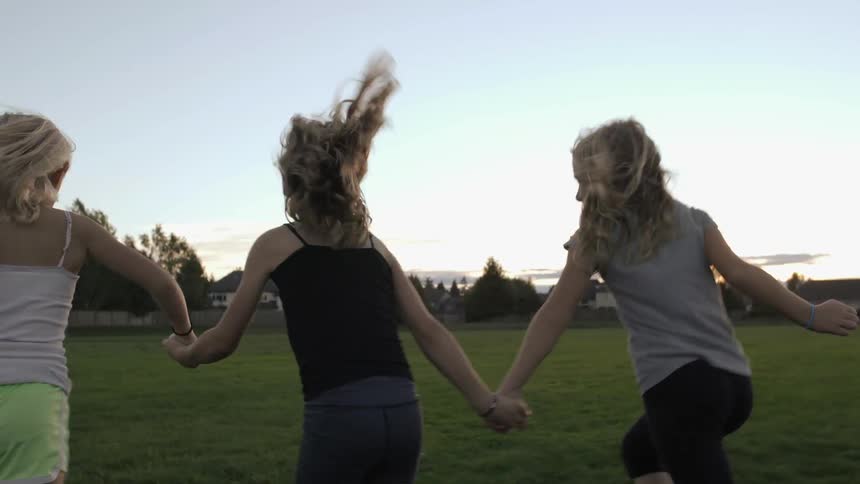 Three girls hold hands and run through a grassy field