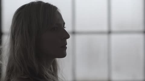 A woman stands in front of a paned window