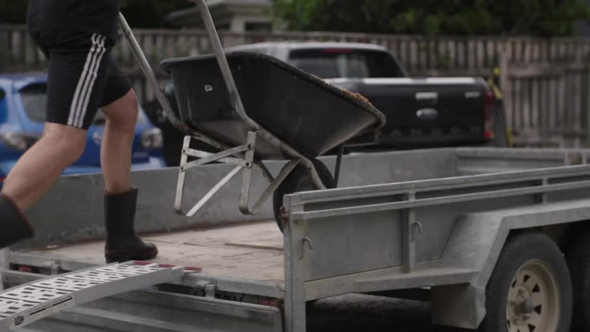 Man dumping a wheelbarrow of dirt onto a trailer