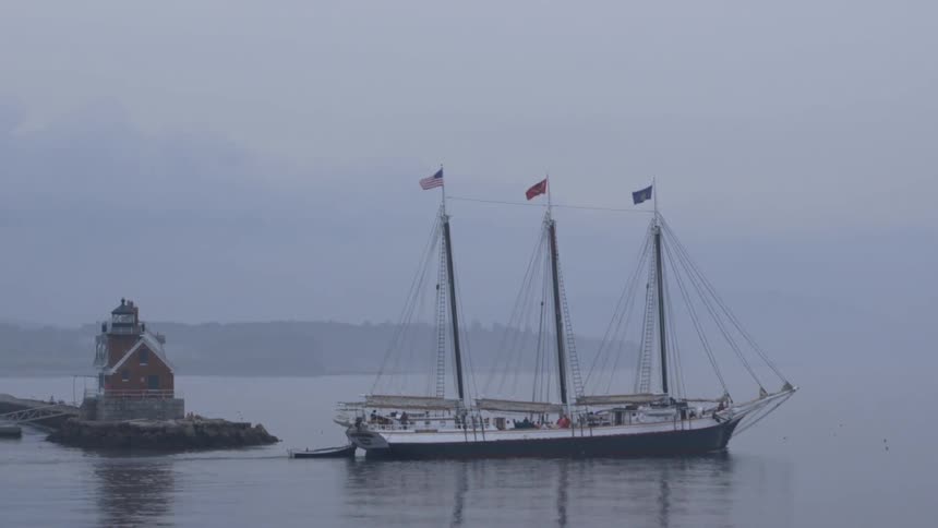 A ship passing in front of a lighthouse on a very overcast day
