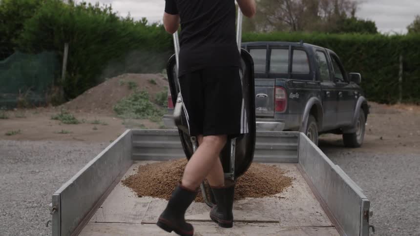 A man pushes and dumps a wheelbarrow into a trailer
