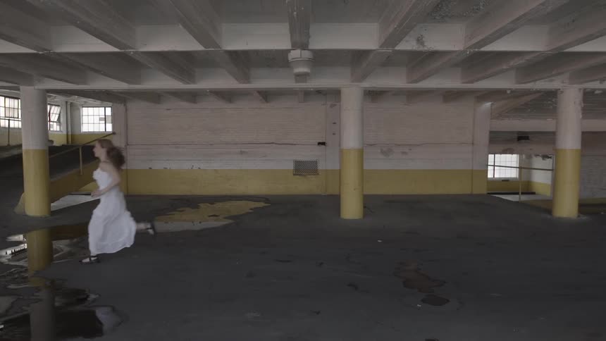 A young woman in a white dress is running in a parking deck