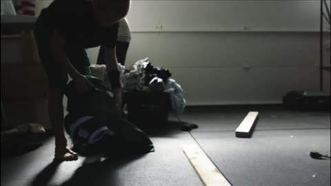 A mother in a garage doing laundry while a boy gets his football gear