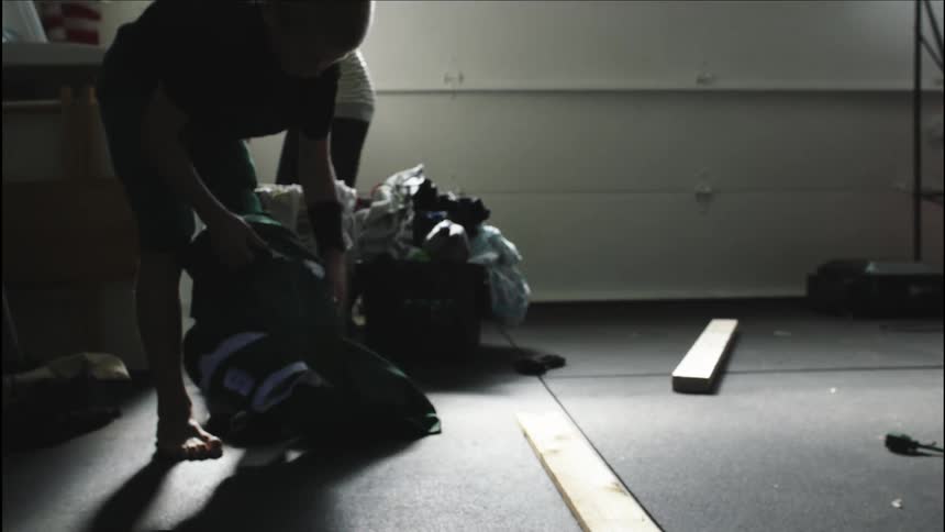 A mother in a garage doing laundry while a boy gets his football gear
