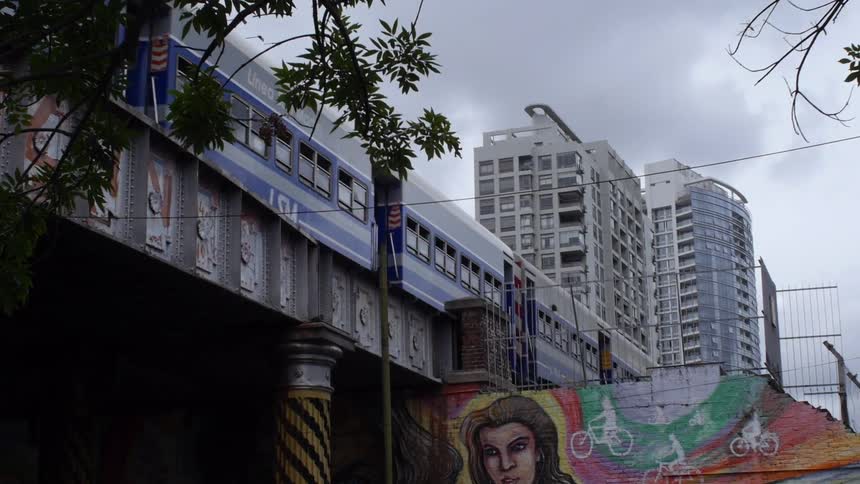 A city train travels above a wall with graffiti art