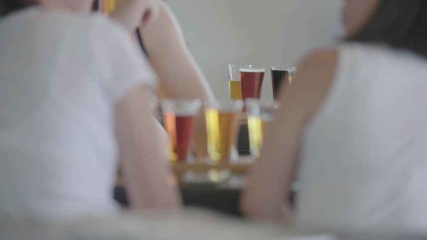 Two woman sit at a bar with beer samples in glasses