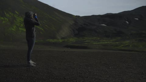 A woman is taking pictures of her view on top of a hill