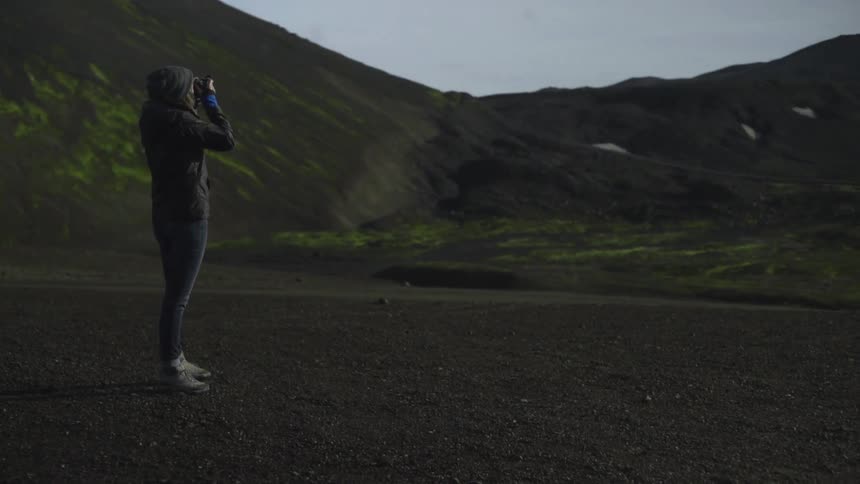 A woman is taking pictures of her view on top of a hill