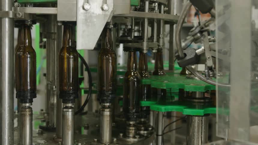 Beer bottles are carried along by machinery in a processing plant