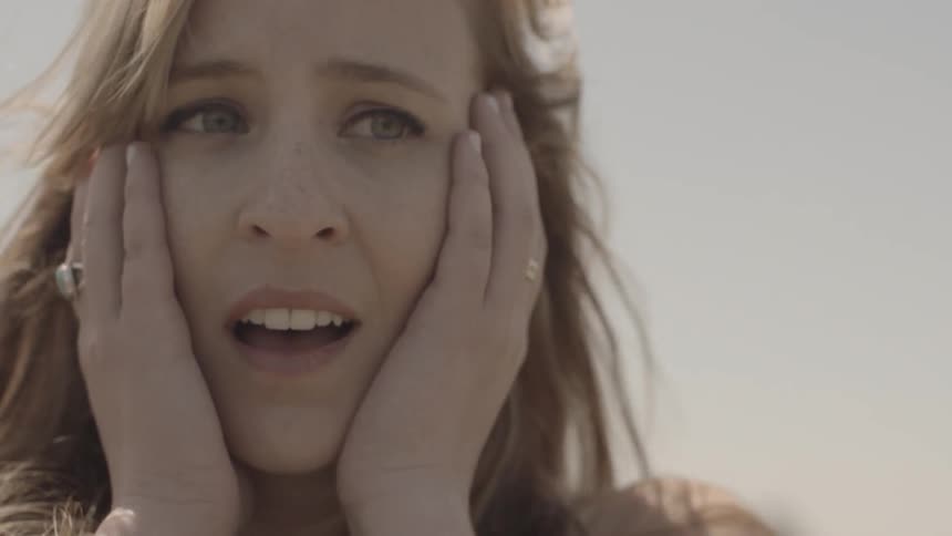 The breeze rustles a woman's hair as she puts her hands on her face and smiles