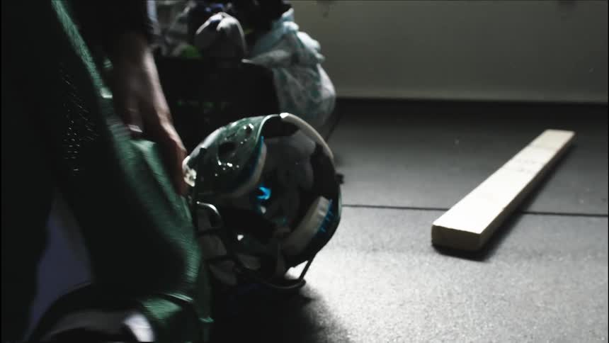 An individual rolling and lifting shoulder pads covered with a football jersey , bumping a football helmet that was resting on the floor