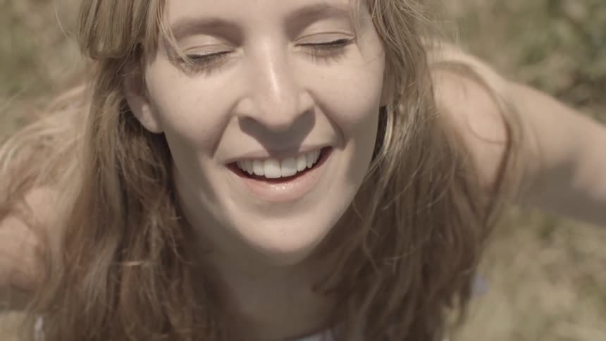 A young, white, blonde woman looks up toward the sun with closed eyes, smiling