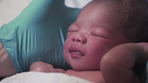 Gloved hands hold a newborn baby