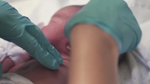 A nurse putting a thermometer in the ear of a newborn