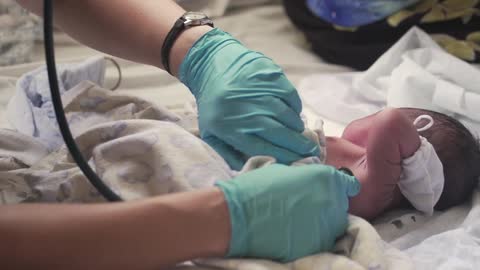 A nurse checks the heartbeat of a newborn with a stethoscope