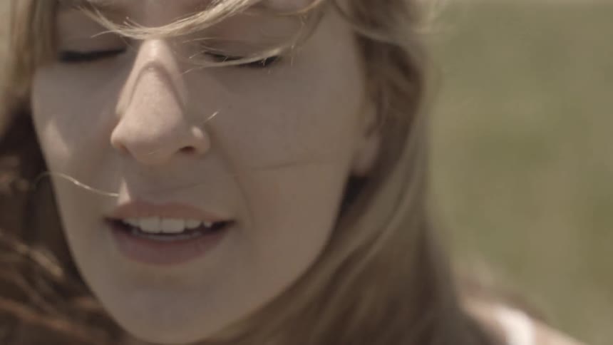 A young blonde woman smiling and looking round before closing her eyes as a breeze blows her hair