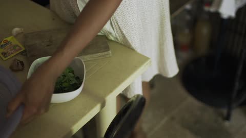 A dark skinned woman in a white dress prepares a dish of food