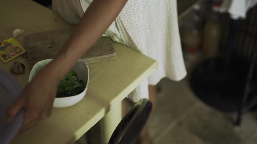 A dark skinned woman in a white dress prepares a dish of food
