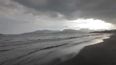 Waves crashing onto a beach under a cloudy sky