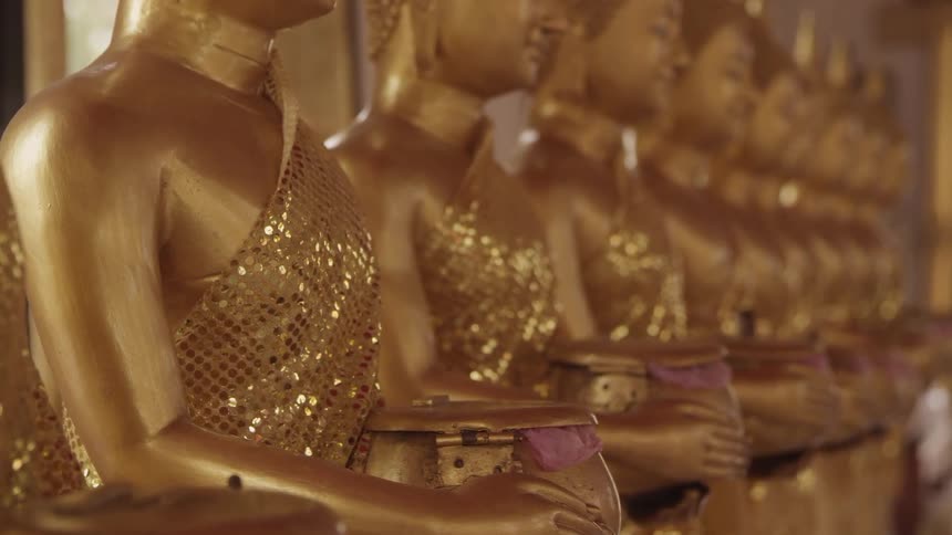 Golden statues clothed in sequined golden clothing while holding gold pots with bits of light purple cloth peeking out from under the lids