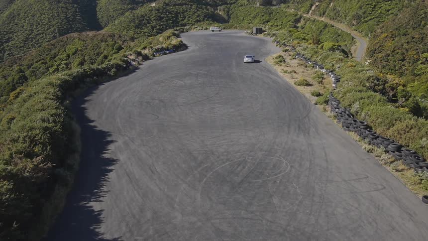 A car drives on a paved lot atop a lush green mountain