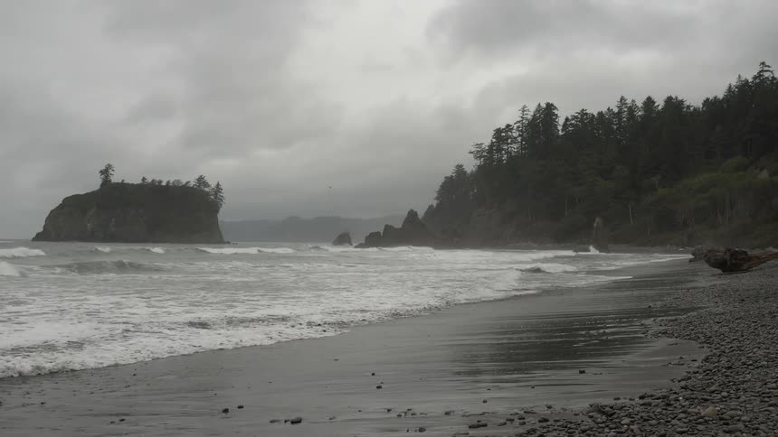 Waves crash against a beach on a foggy evening