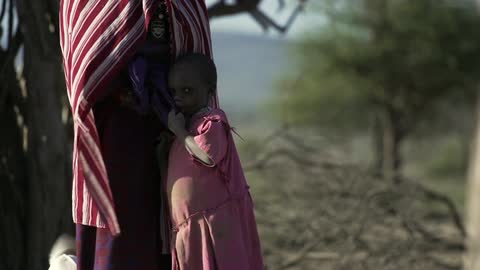 Child leans against mother outdoors near tree