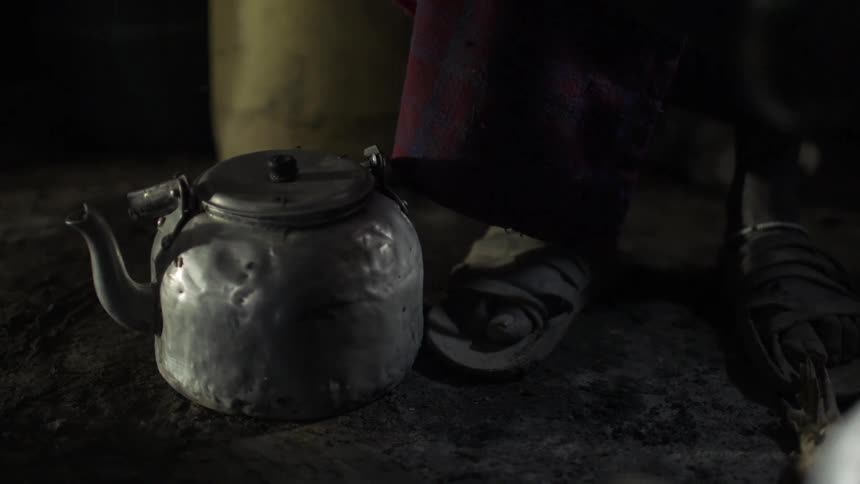 A tea kettle surrounded by flies sits at someone's feet