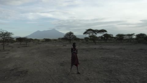 A young boy standing in a dirt field as another boy walks up and joins him