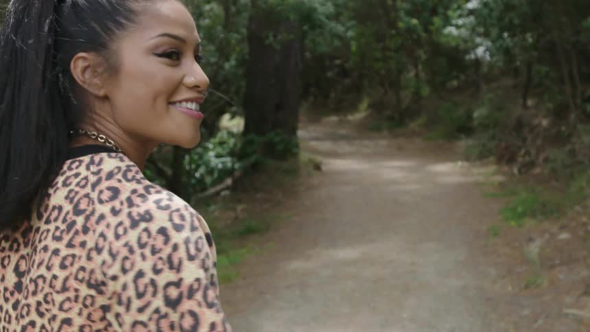 A smiling woman walks down a forest trail