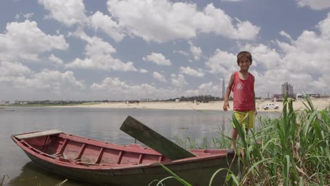 A boy balances on a boat and waves