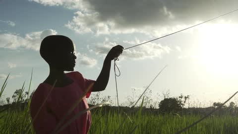 A girl wearing a pink dress, holding the end of a string and standing in tall grass