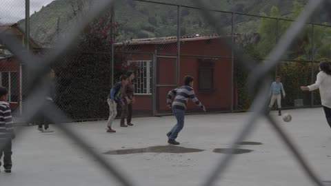 Children and their teacher play soccer in a fenced in school yard