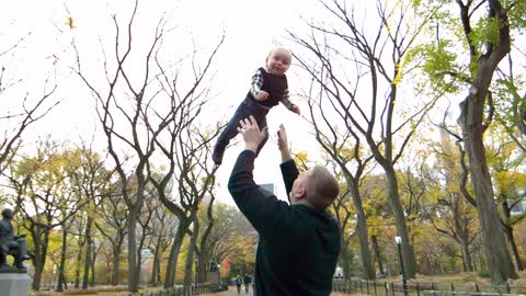 Man holding baby up high in the middle of a park