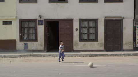A boy kicks a ball in the street