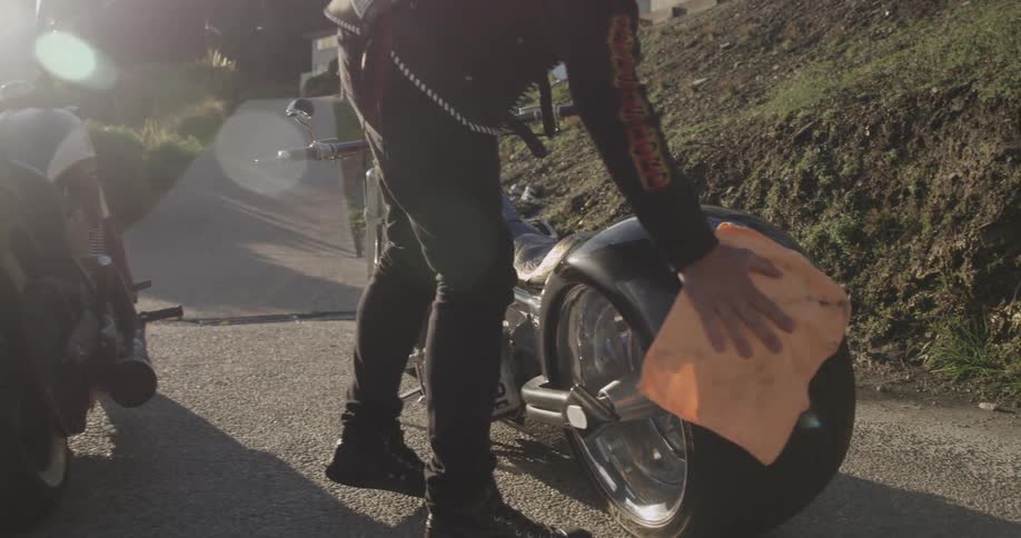 Man in a leather coat shining a motorcycle with a rag