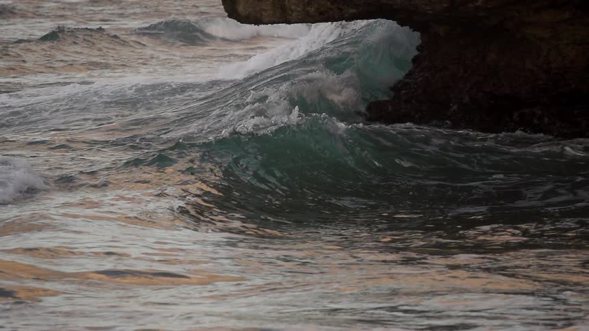 A wave crashes around the base of a rock
