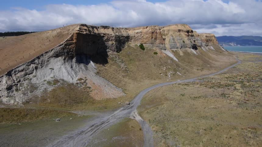 A dirt road runs path a cliff and towards the ocean