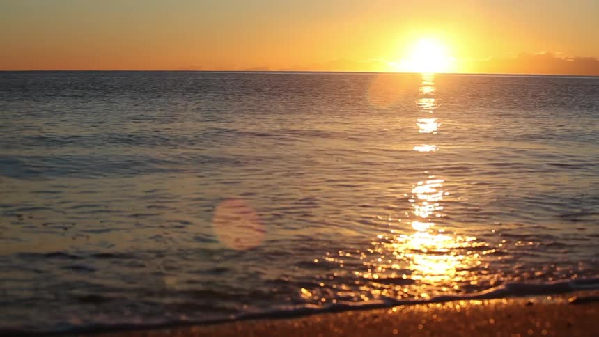 The sun sets over the ocean as waves wash up on the beach