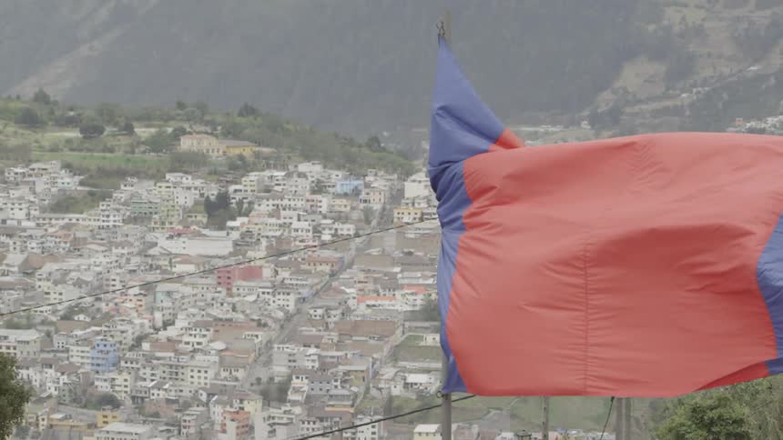 Large flag waving in the wind with a city in the background