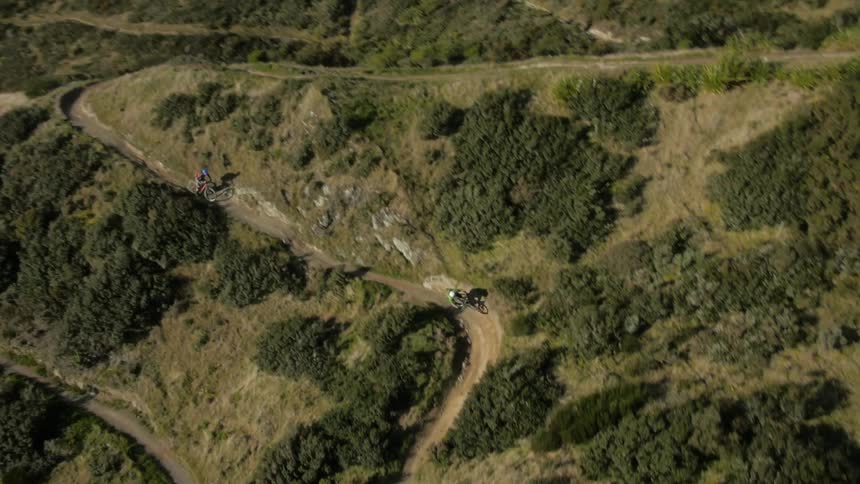 Three people riding bicycles along a winding dirt coarse down a hillside set in the mountains