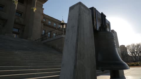 A large bell swings back in forth in front of a building
