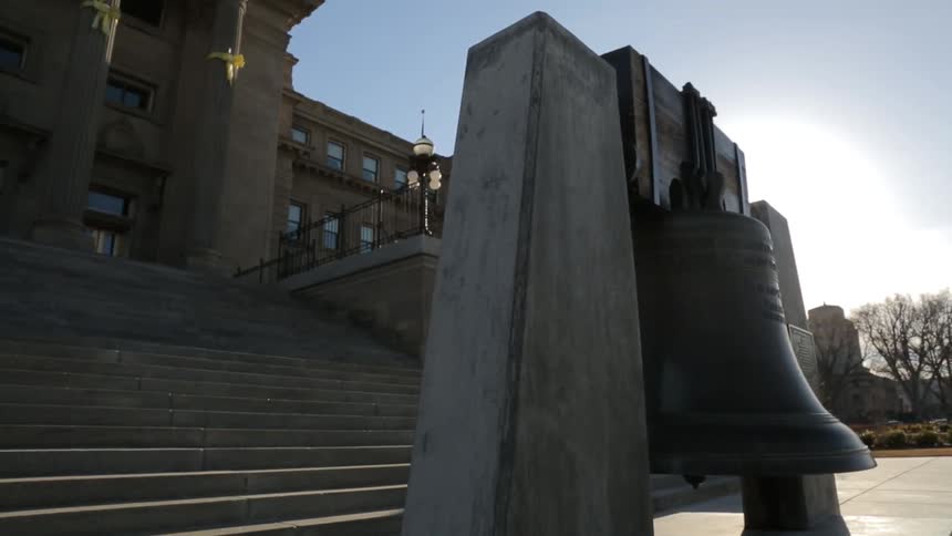 A large bell swings back in forth in front of a building